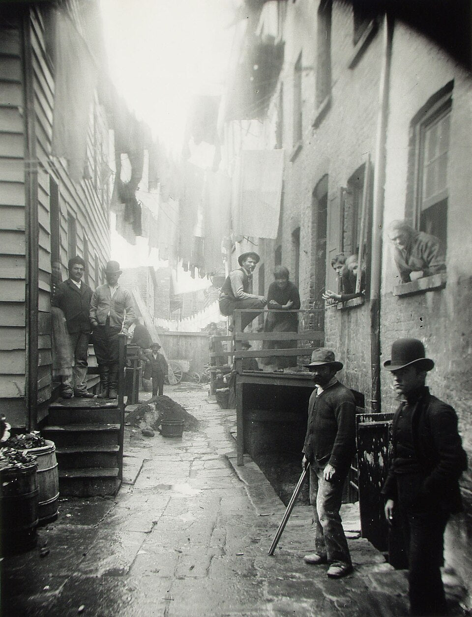 Jacob Riis’s Bandits’ Roost, 59 1/2 Mulberry Street (1888), showing men, residents and a child in a narrow Lower Manhattan tenement alley.